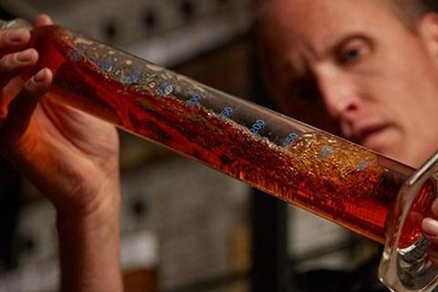 A person holding a large tube filled with liquid, presumably whisky, for a blending class.
