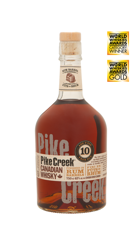 Pike Creek Double Barreled Canadian Whisky 750ml bottle featuring a clear glass bottle with a wooden cap and a dark label accented with copper and cream tones. The label highlights the double-barrel aging process, including finishing in rum barrels. The whisky inside has a rich amber hue. A smooth and complex Canadian whisky crafted in Ontario, with notes of honeycomb toffee, molasses, vanilla, and lingering rye spice.